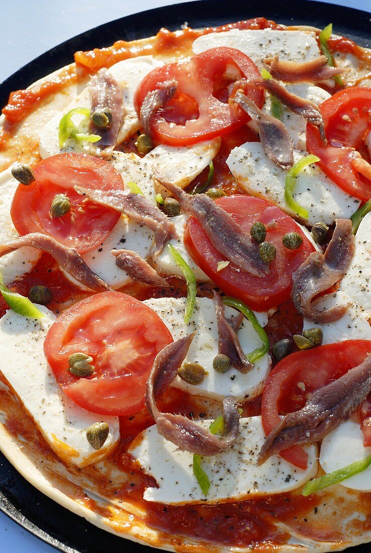 Pizza topped with tomatoes, capers and anchovies (unbaked)