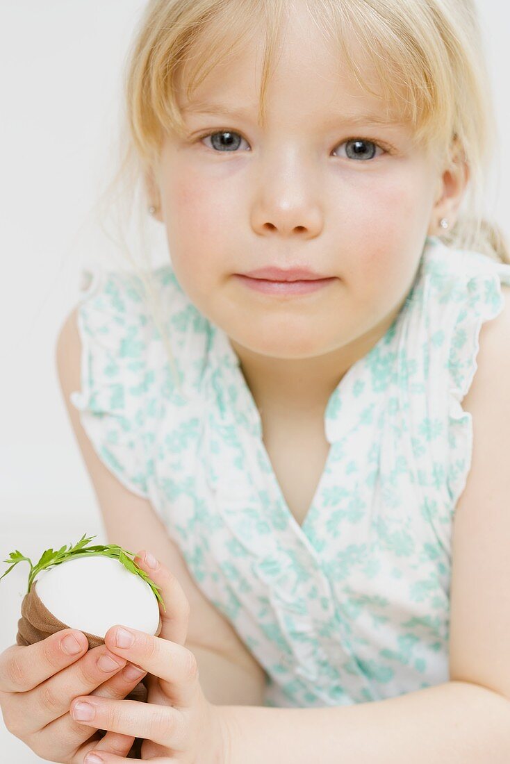 Little girl holding egg with parsley & stocking (for dyeing)