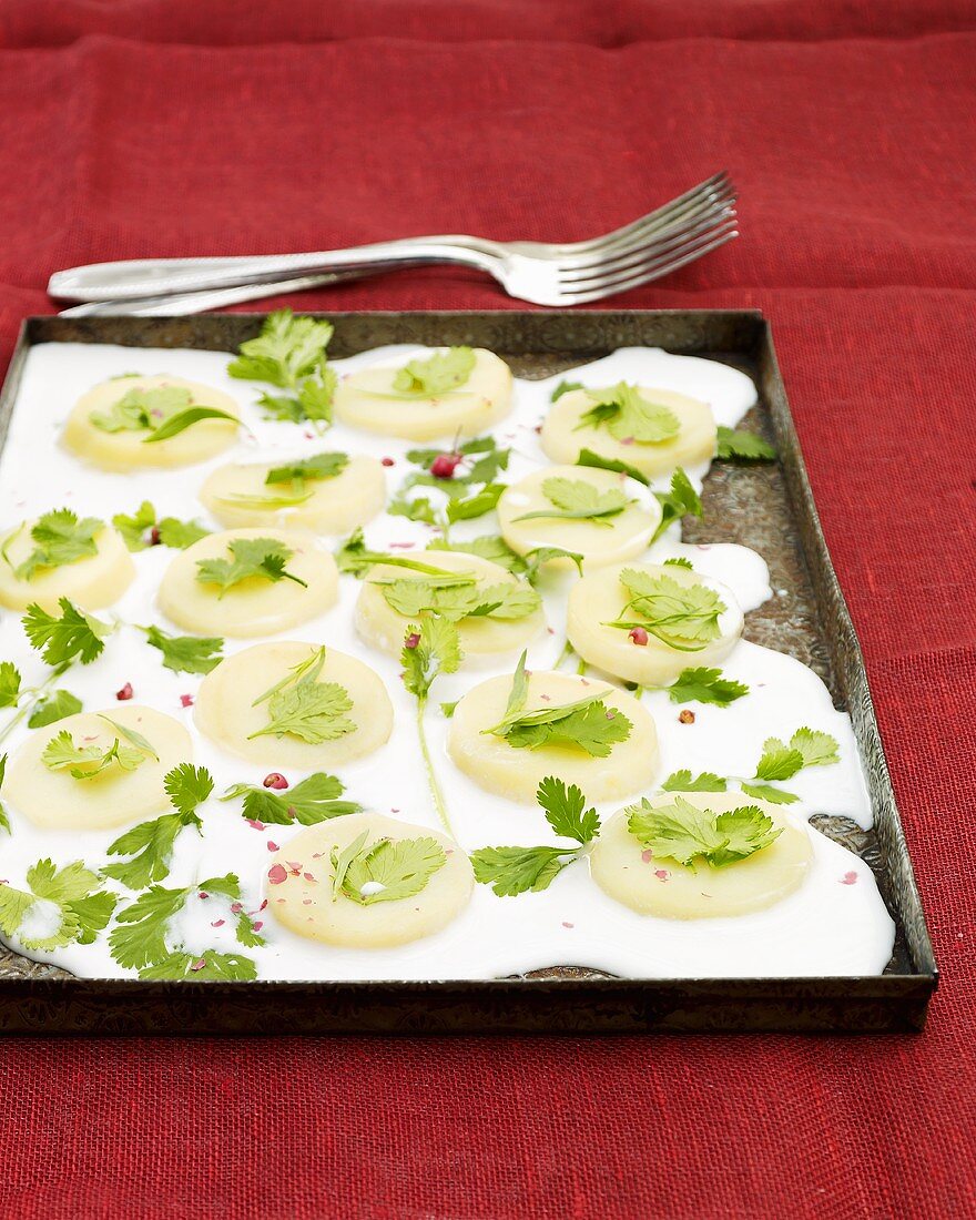 Potato slices with coconut milk and coriander on baking tray