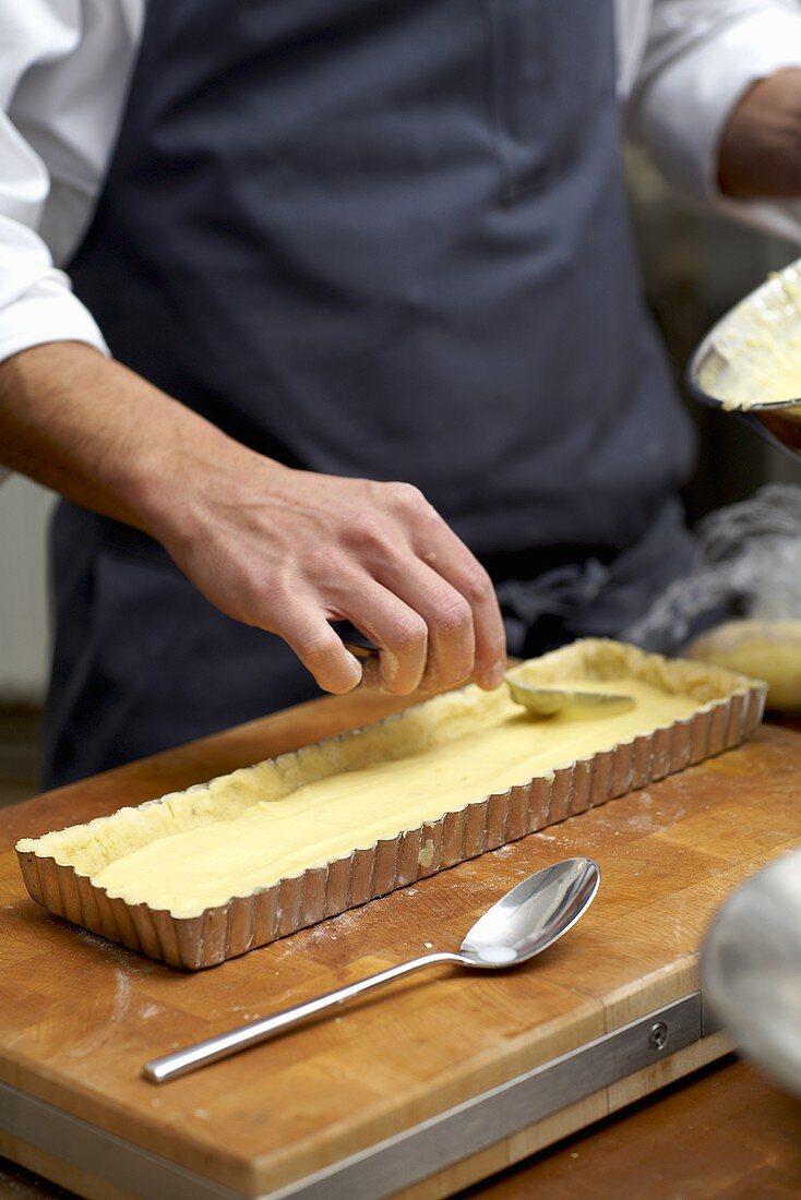 Spreading cream in a tart tin lined with pastry