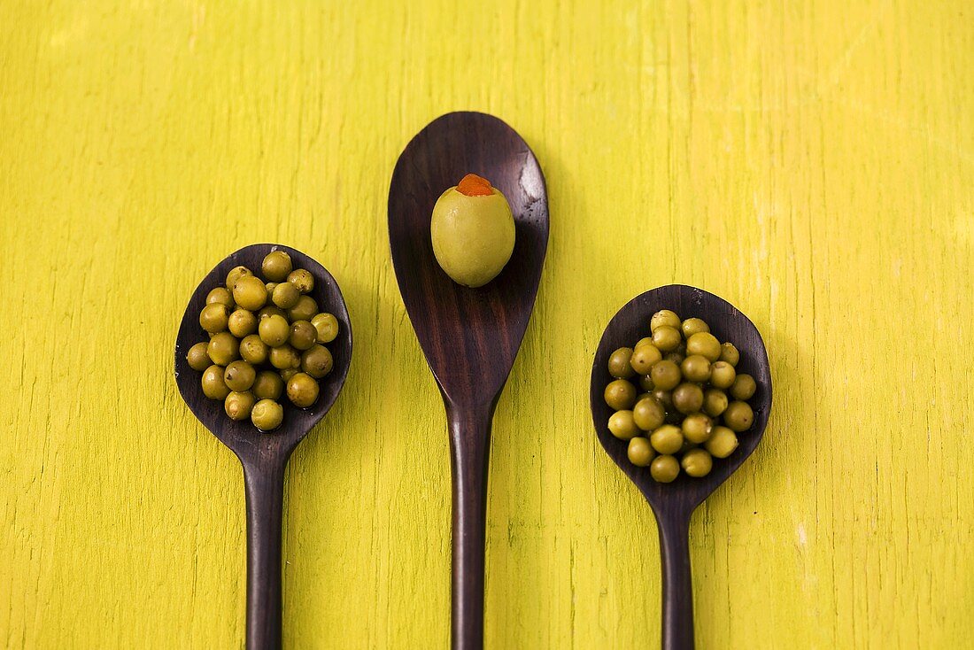 Stuffed olive and green peppercorns on three wooden spoons