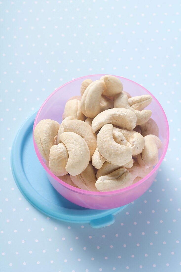 Shelled cashew nuts in Tupperware container on spotted background