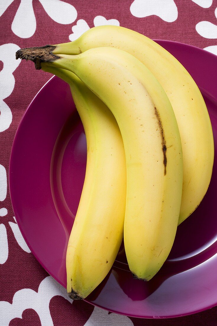 Drei Bananen auf violettem Teller