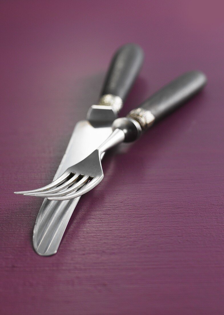 Messer und Gabel mit Holzgriff auf lila Holzunterrgund