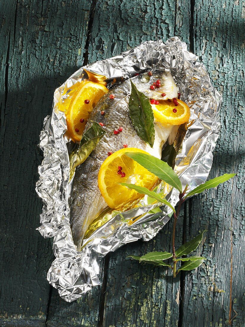 Sea bream with orange slices & bay leaves in aluminium foil