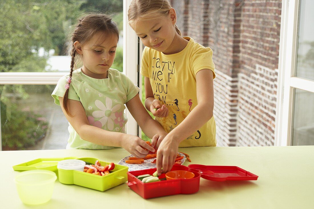 Two girls putting vegetable sticks into lunch boxes
