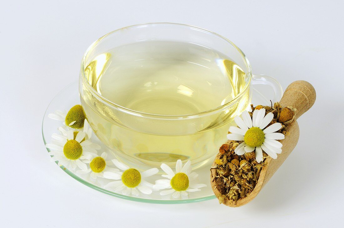 Chamomile tea in glass cup and saucer with flowers