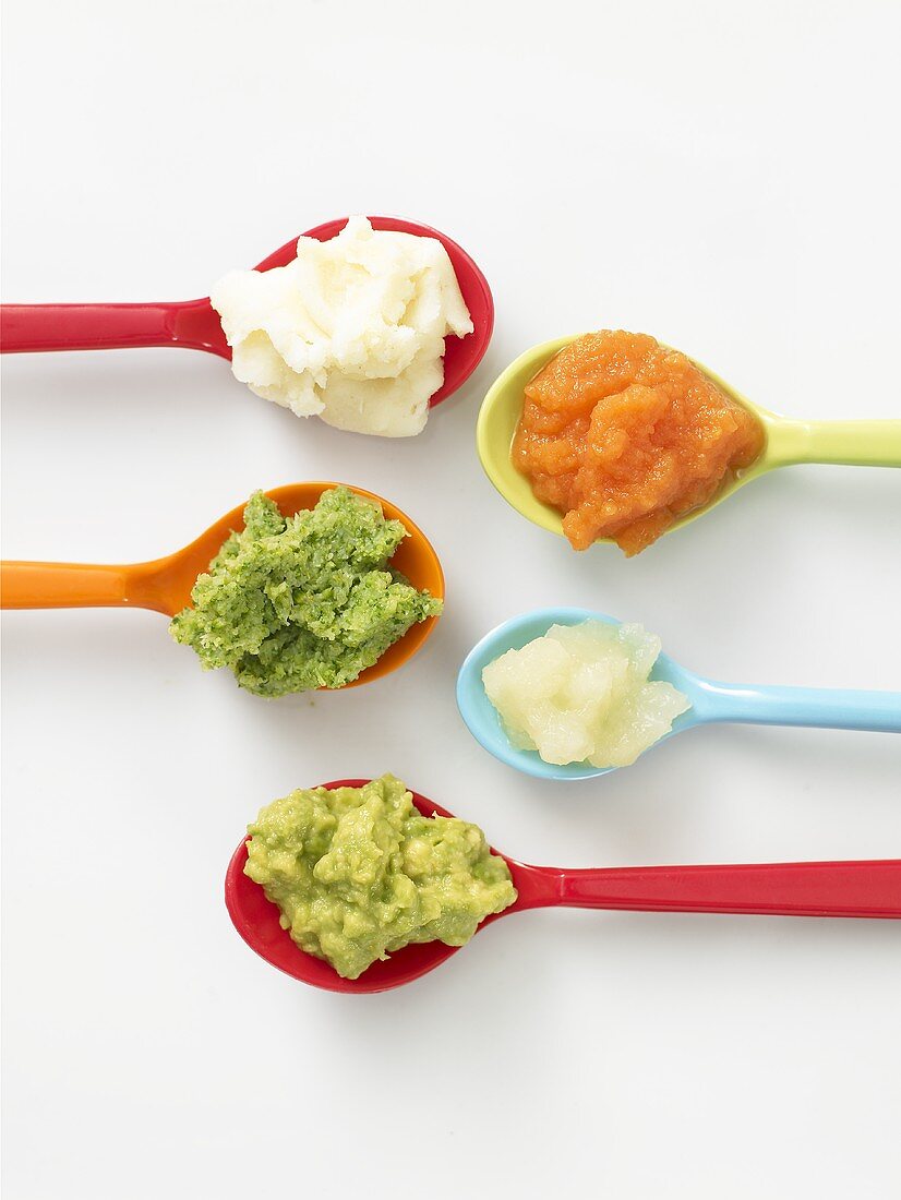 Different vegetable purees on coloured spoons (overhead)