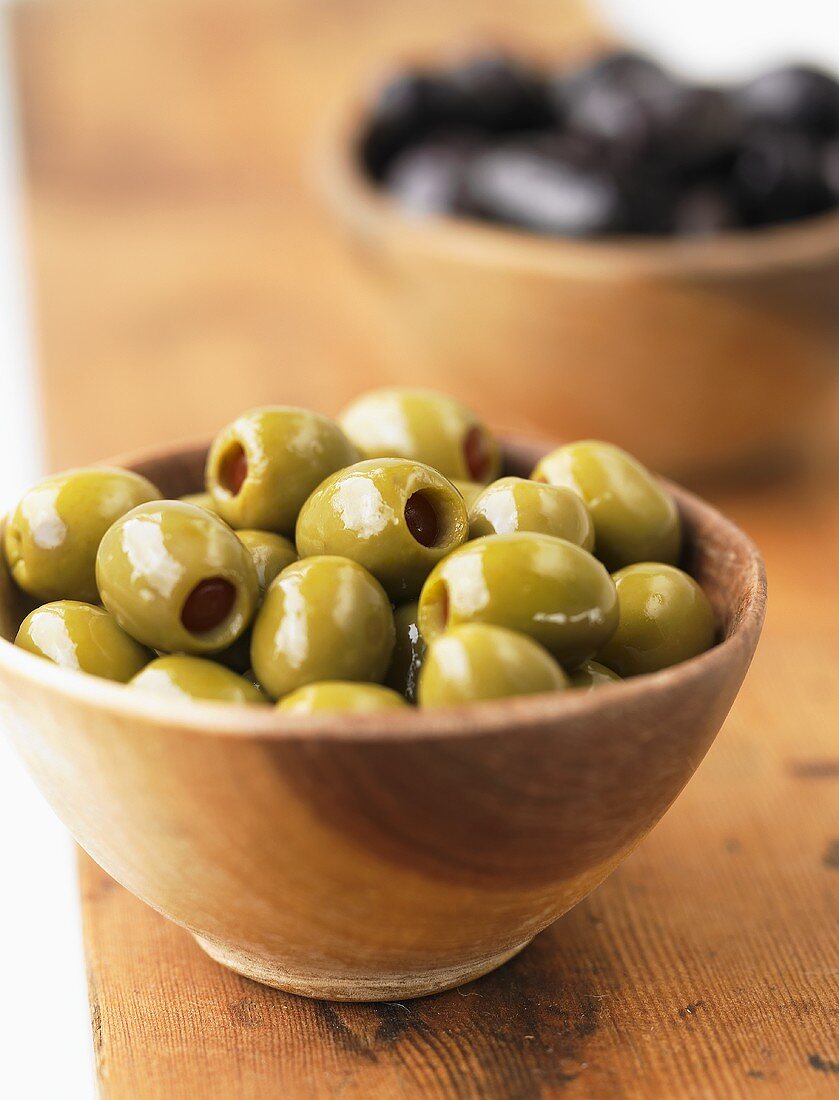A wooden bowl full of green olives