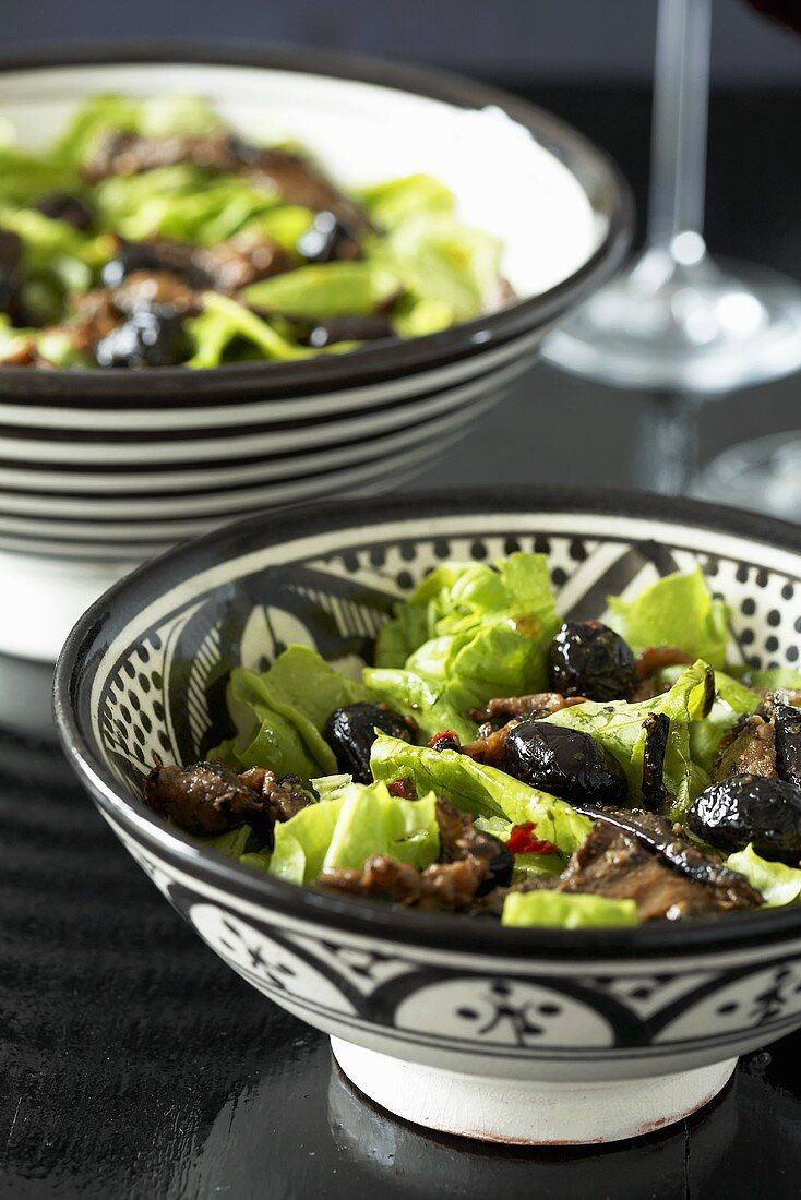Two bowls of lettuce with roasted vegetables and olives