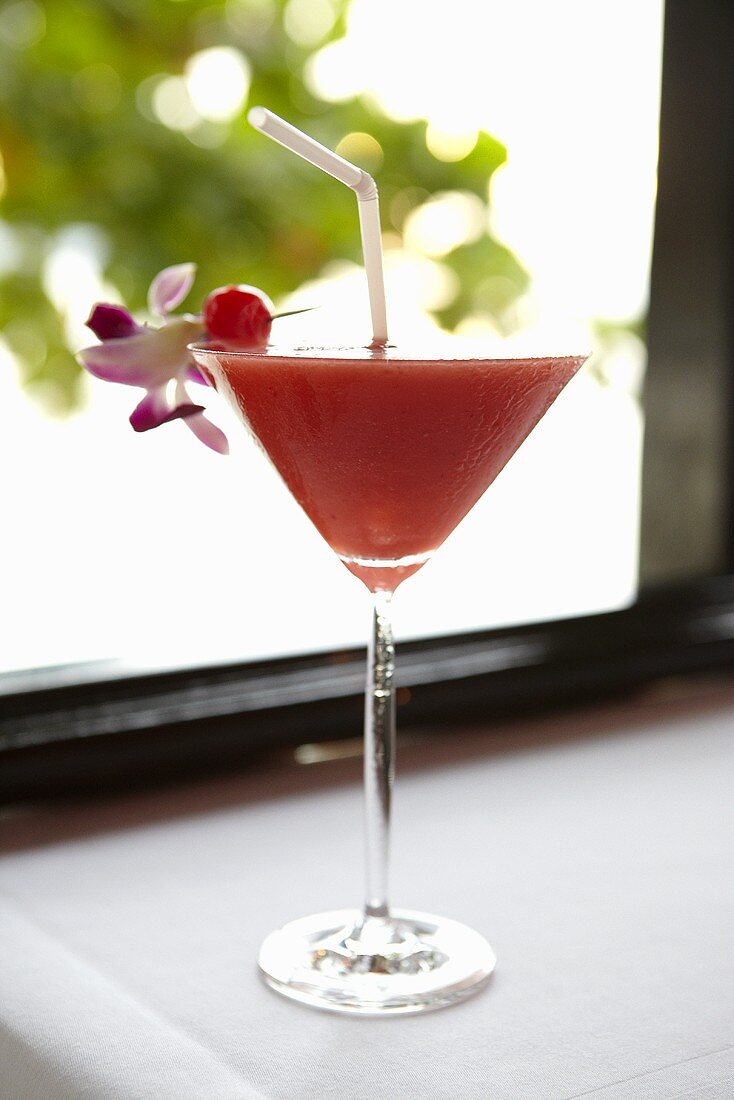 Fruity cocktail with straw in front of window