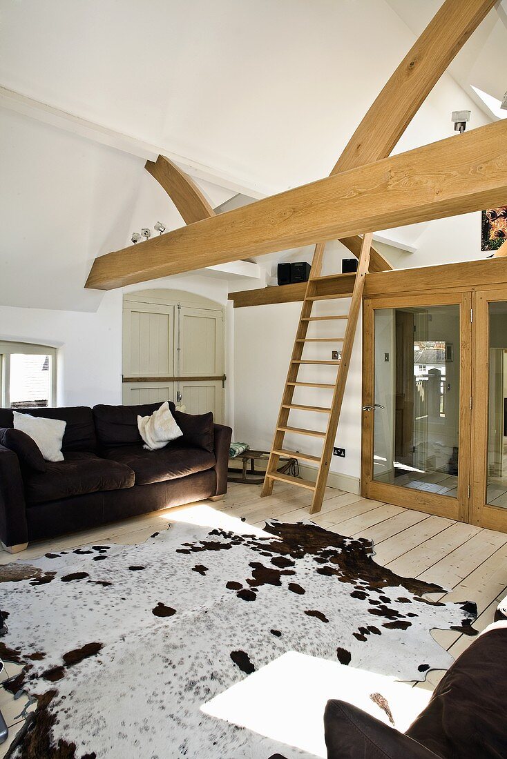 Wohnzimmer im Dachgeschoss mit Balkendecke, Couch, Kuhfell & Holzleiter zu kleiner Galerie