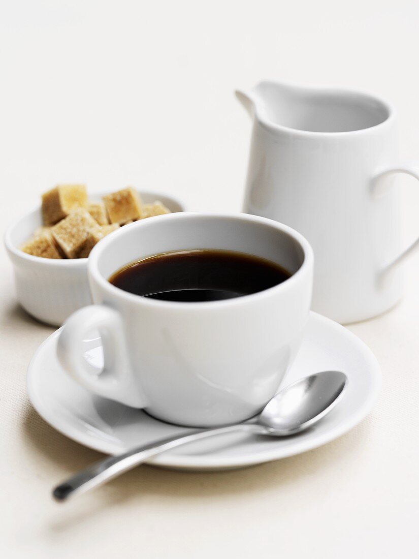 A cup of black coffee, sugar cubes and milk jug