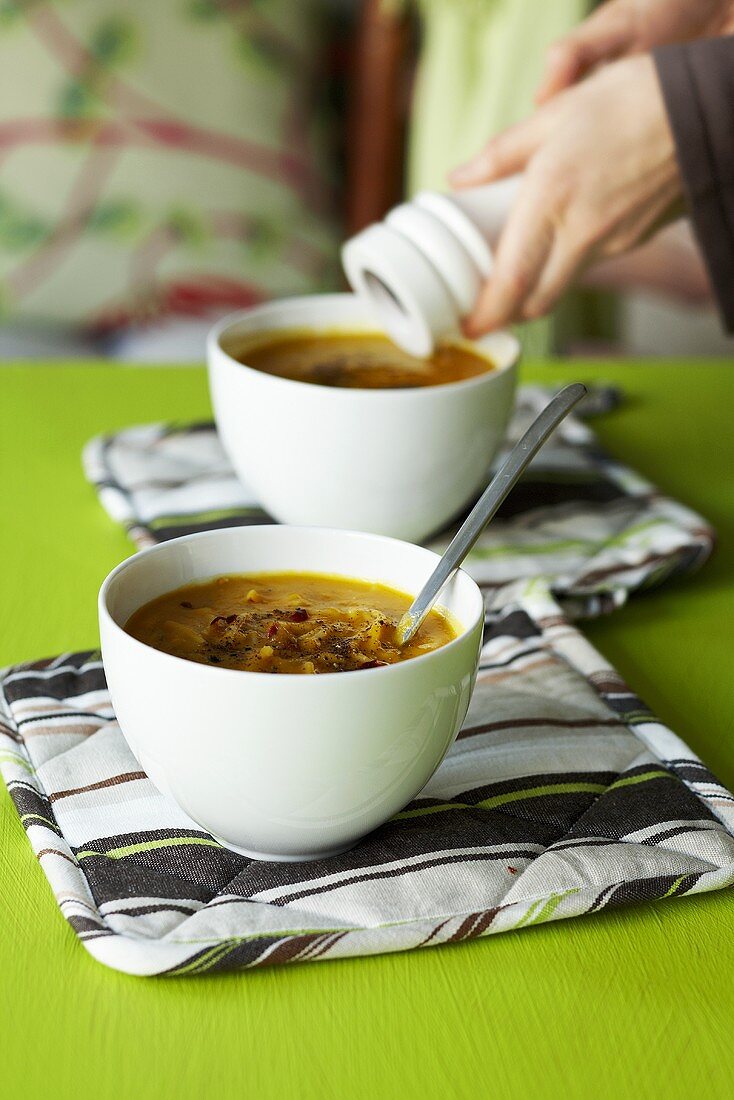 Frau würzt Kürbis-Nudelsuppe mit Pfeffer aus der Mühle