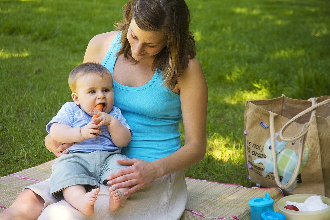 Baby isst Möhre beim Picknick mit seiner Mutter