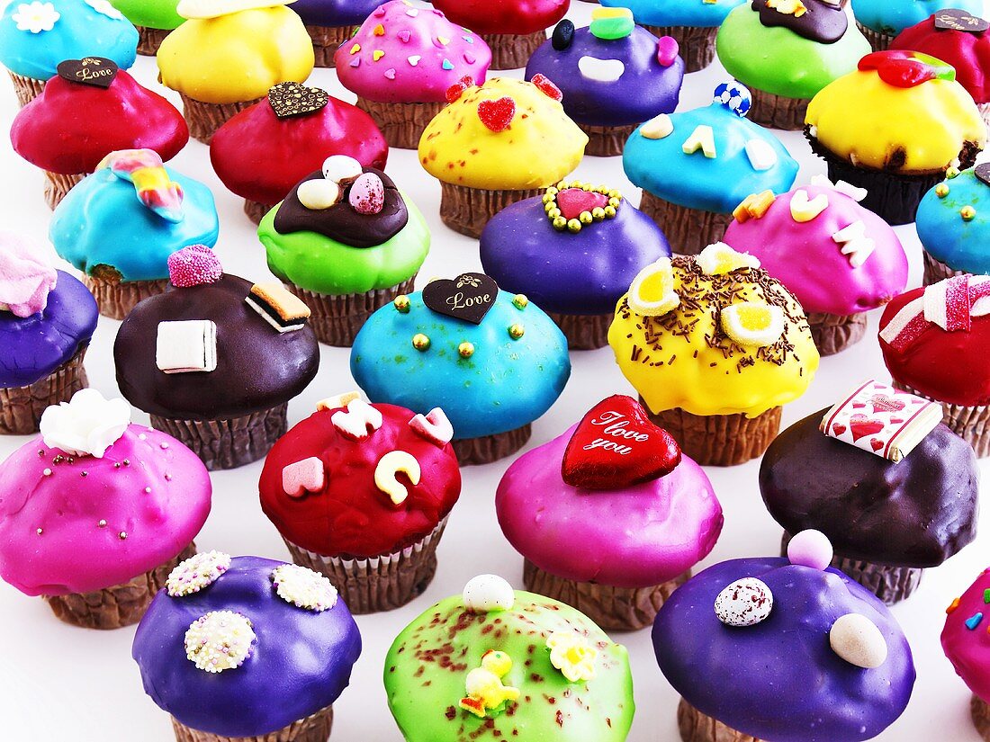 Many muffins with coloured icing and decorations