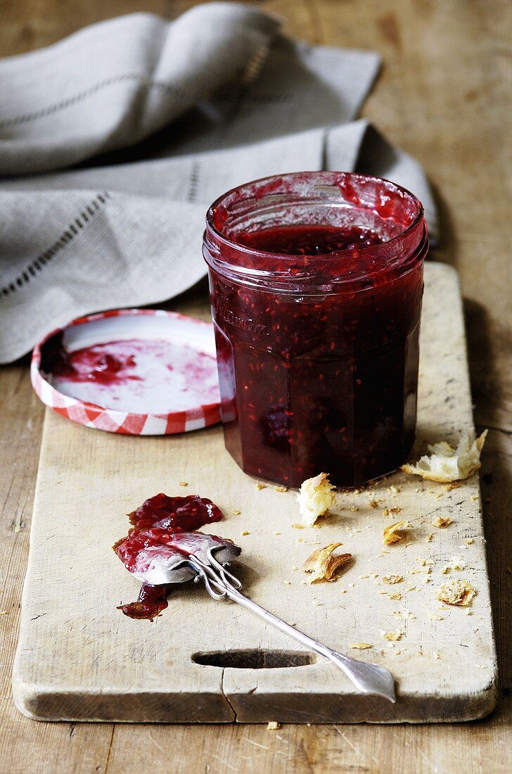 Raspberry jam in jar, breadcrumbs and spoon on board