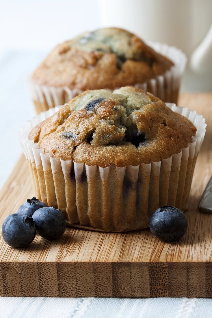 Two blueberry muffins on chopping board