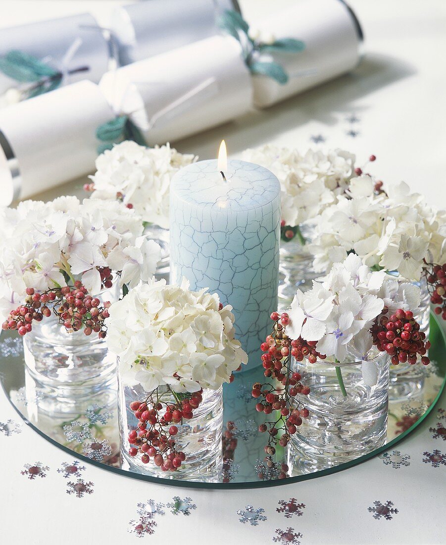 Blaue Kerze und Gläser mit Blumendeko auf Spiegel
