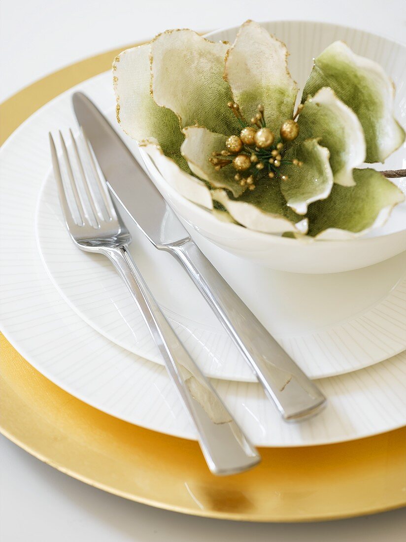 Place-setting with gold underplate, white plates, cutlery and flower