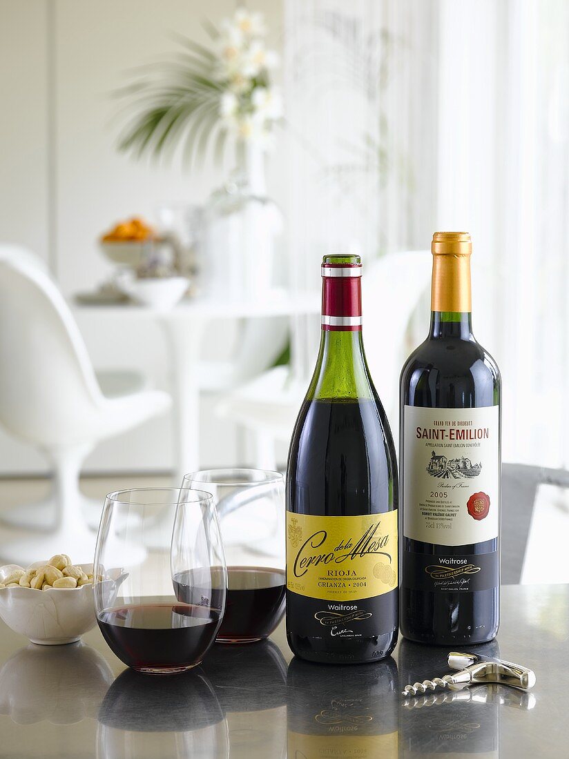 Offene Rotweinflaschen, Weingläser und Korkenzieher auf Tisch