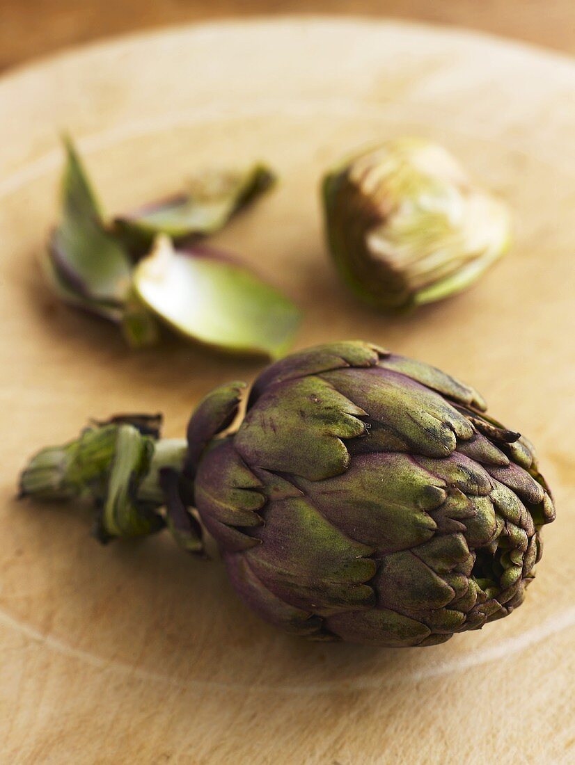 Whole and trimmed artichoke on wooden board