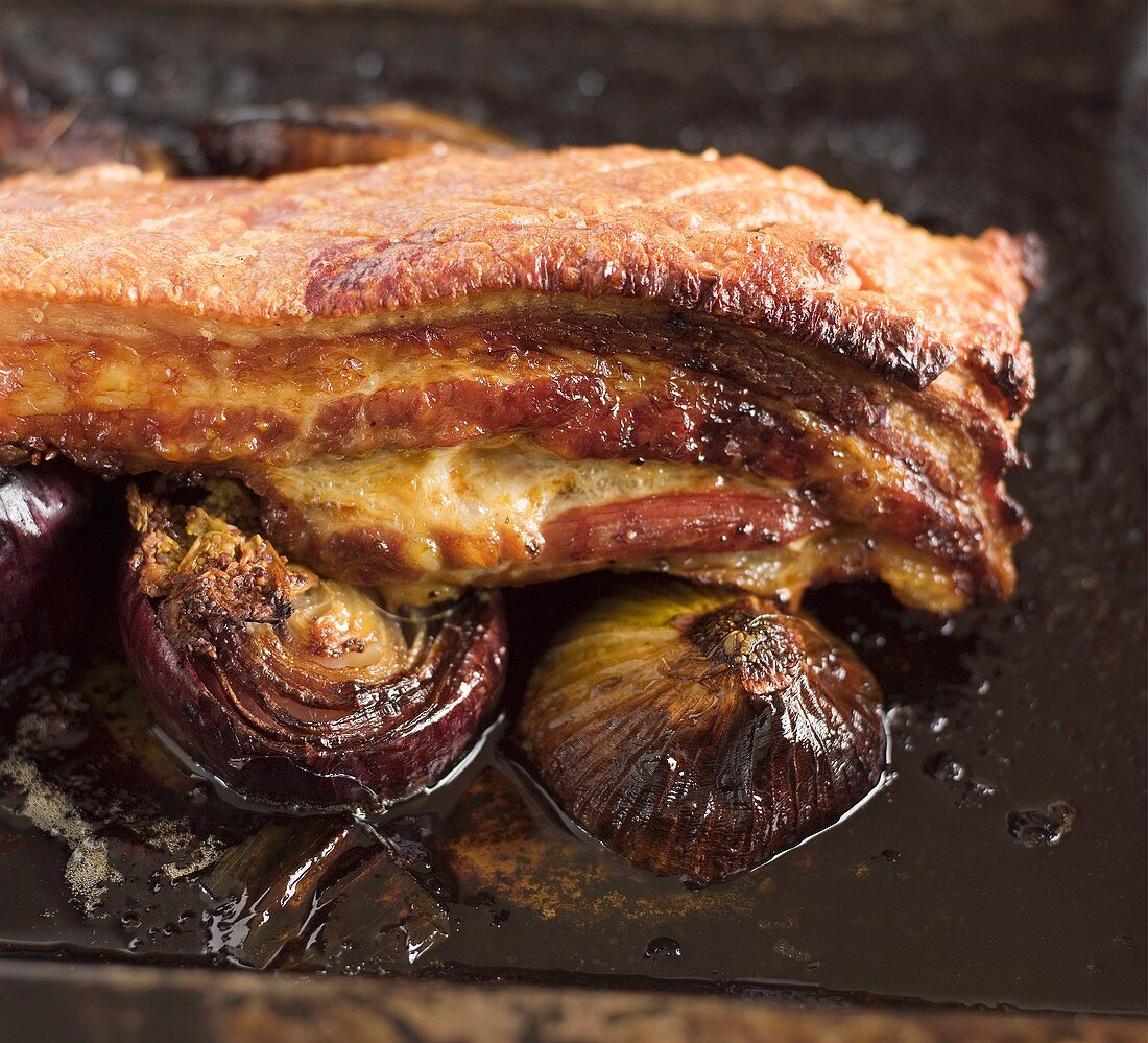 Gebratener Schweinebauch mit Zwiebeln auf Backblech