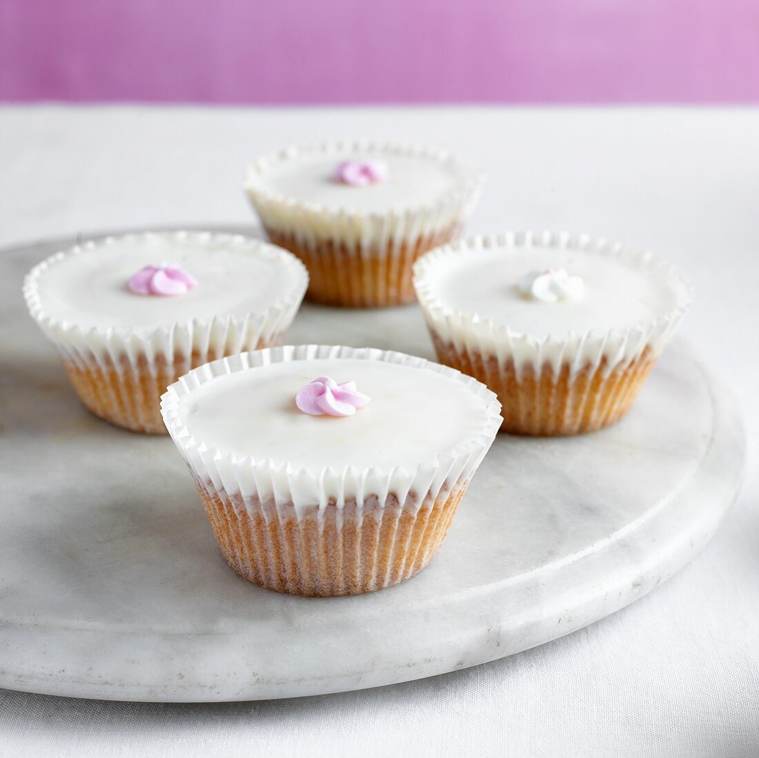 Vier Cupcakes mit Zuckerblumen auf Marmorteller