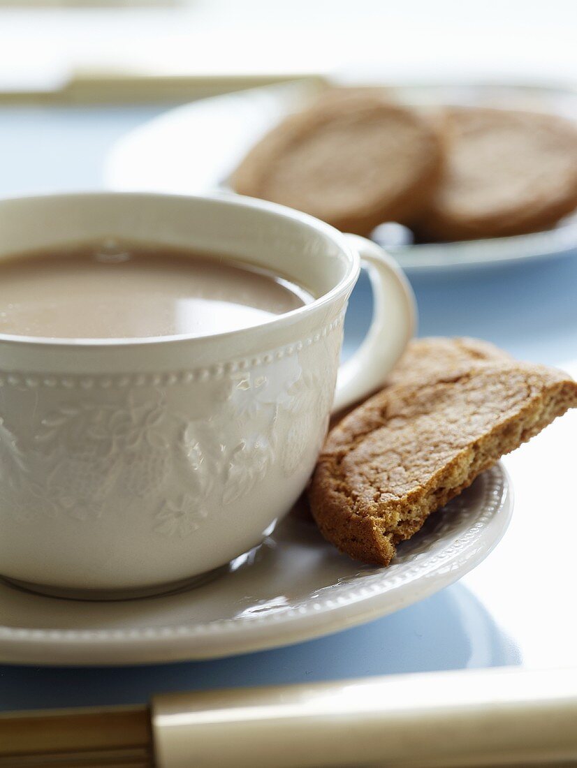 Tea with milk in cup and saucer, biscuits in saucer
