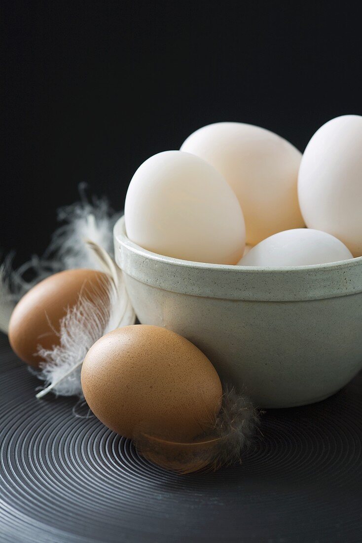 Duck eggs in ceramic basin, hens' eggs with feathers beside it