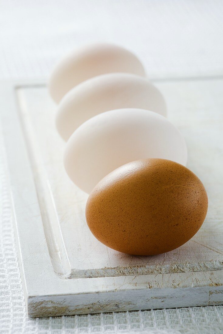 Three duck eggs and a hen's egg on chopping board