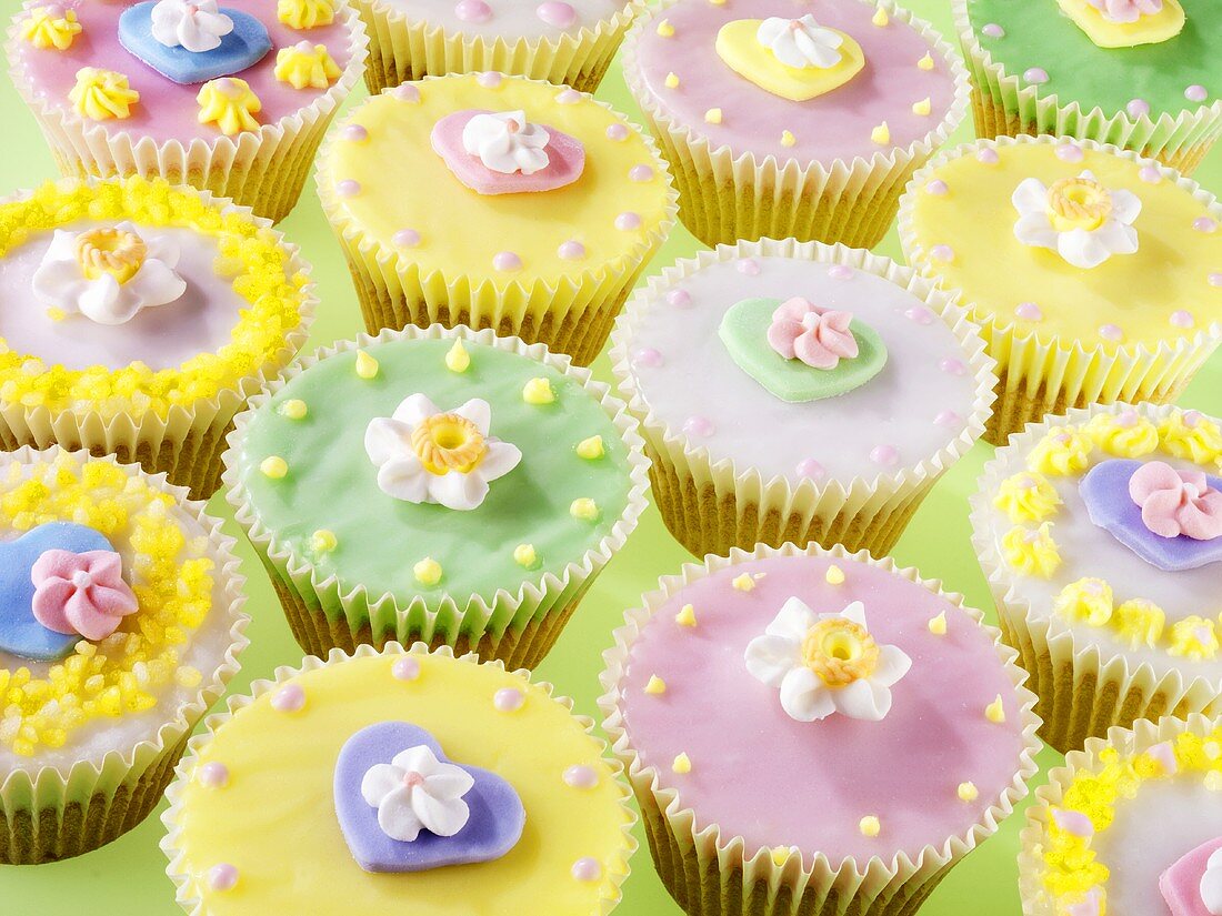 Lots of pastel-coloured fairy cakes decorated with sugar flowers