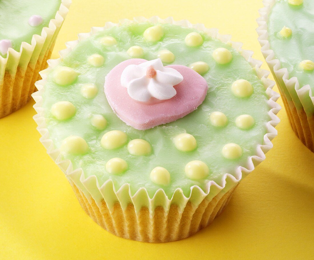 Cupcake mit grüner Glasur, rosa Herz und Zuckerblüte