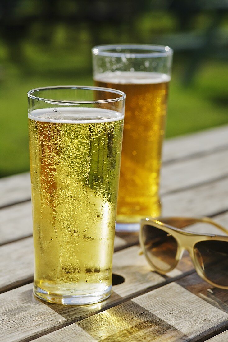 Zwei Gläser Bier auf einem Holztisch im Freien