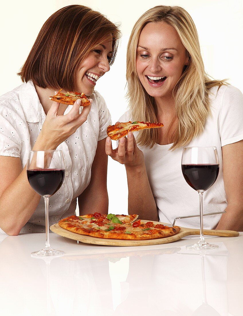 Zwei Frauen unterhalten sich lachend beim Pizzaessen