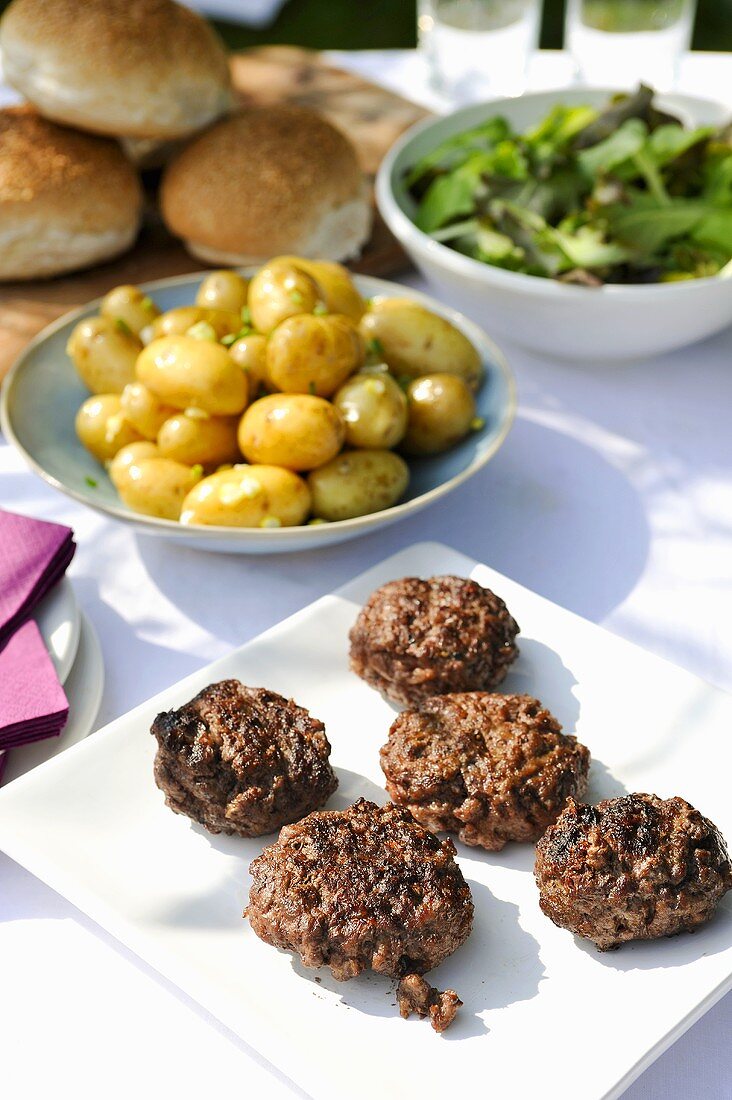 Gegrillte Frikadellen, Pellkartoffeln & Salat auf Tisch