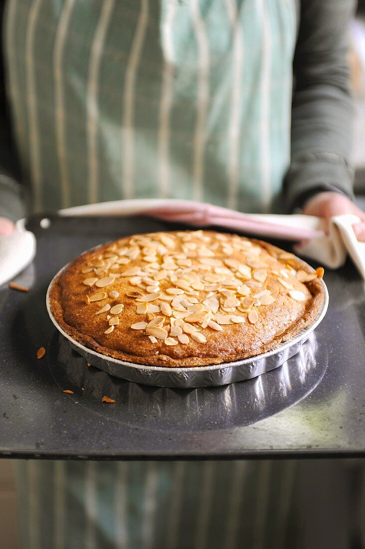 Hands holding a Bakewell Tart on baking tray