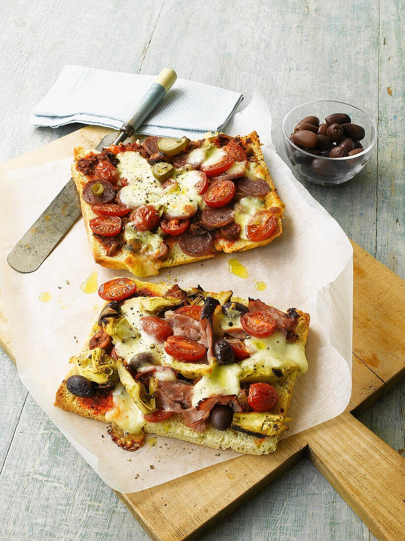 Focaccia-Pizzen mit Oliven, Tomaten, Wurst und Schinken