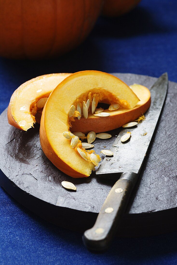 Pumpkin slices, seeds and a knife on a slate platter