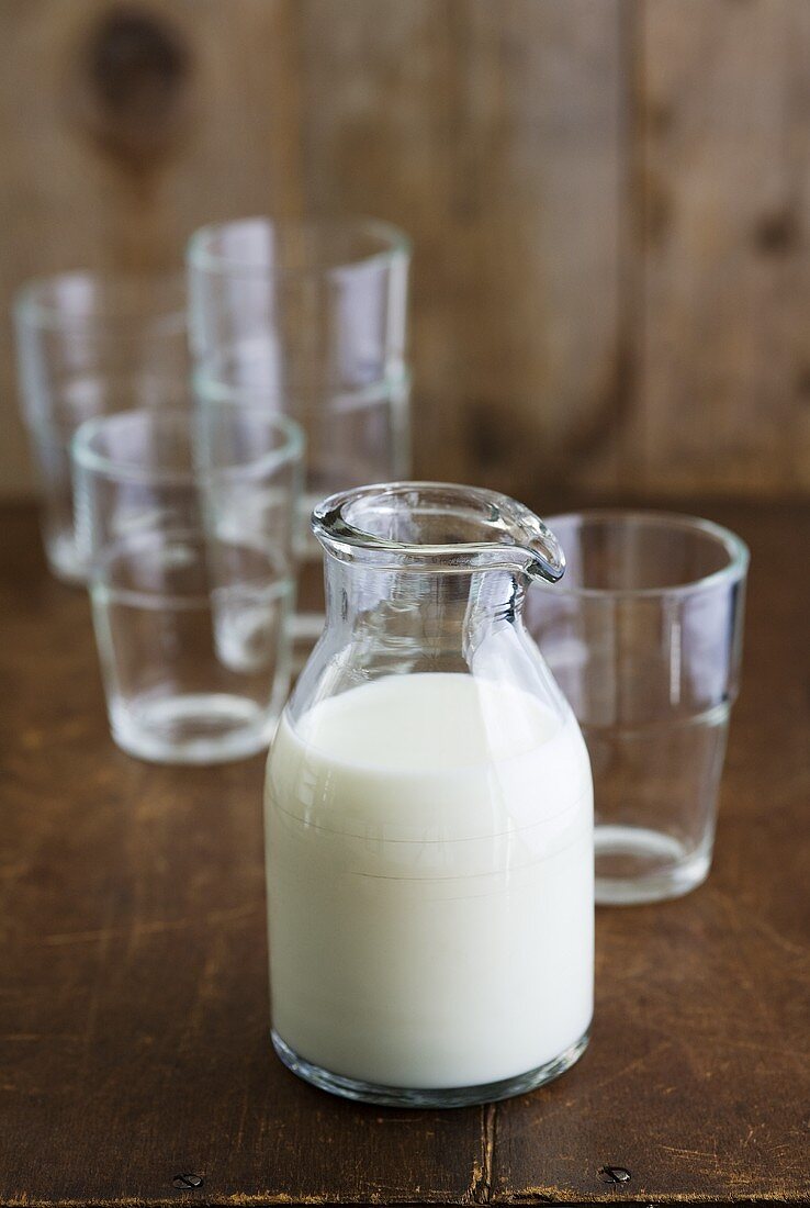 Milch im Glaskrug und leere Trinkgläser