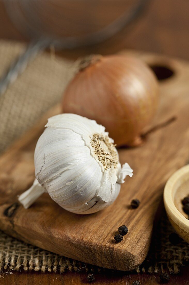 Knoblauch, Zwiebel und Pfefferkörner auf Schneidebrett