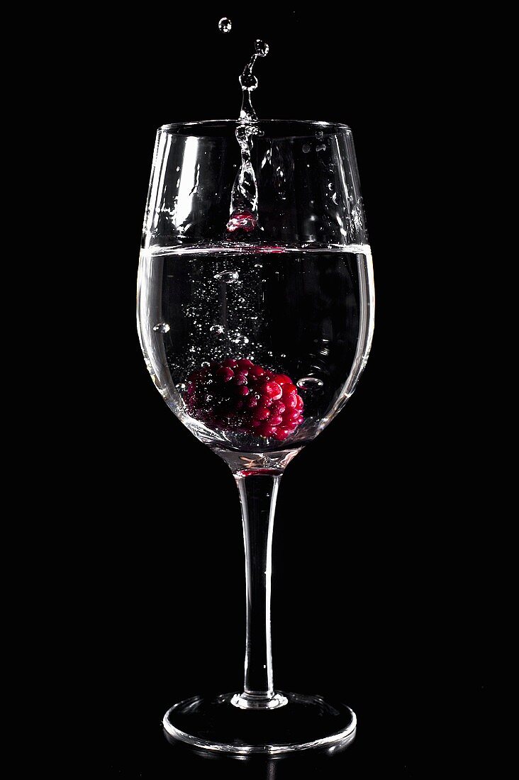 A raspberry falling into a glasss of mineral water
