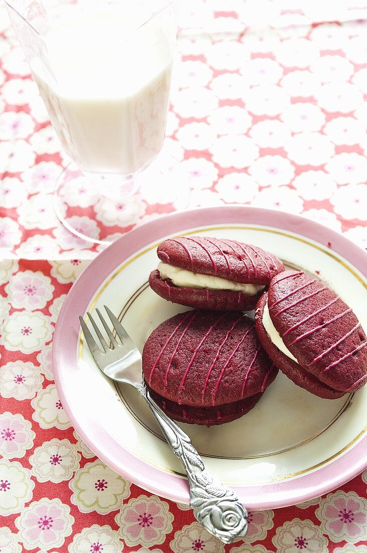 Raspberry whoopie pies on a plate with a fork and a glass of milk