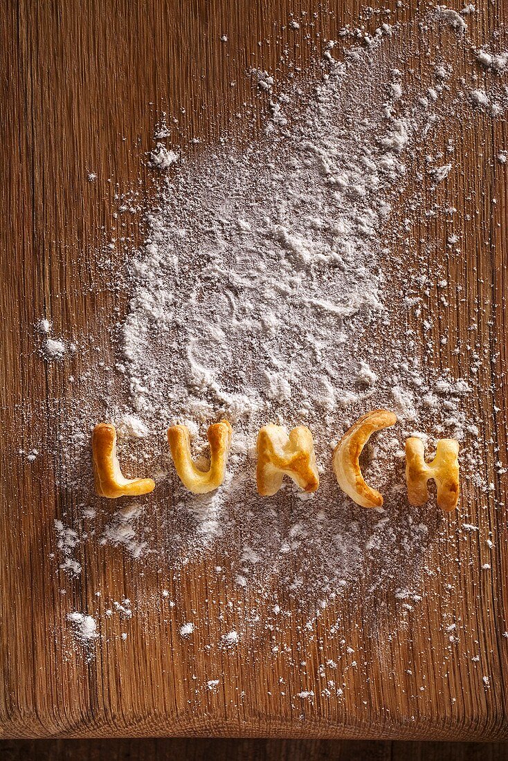 The word 'LUNCH' made out of pastry on a floured wooden board