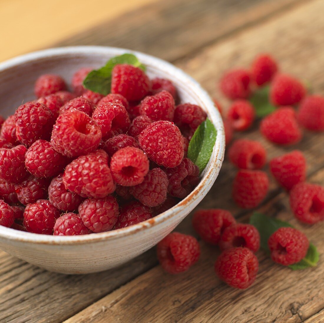 Frische Himbeeren in Schälchen und auf Holztisch