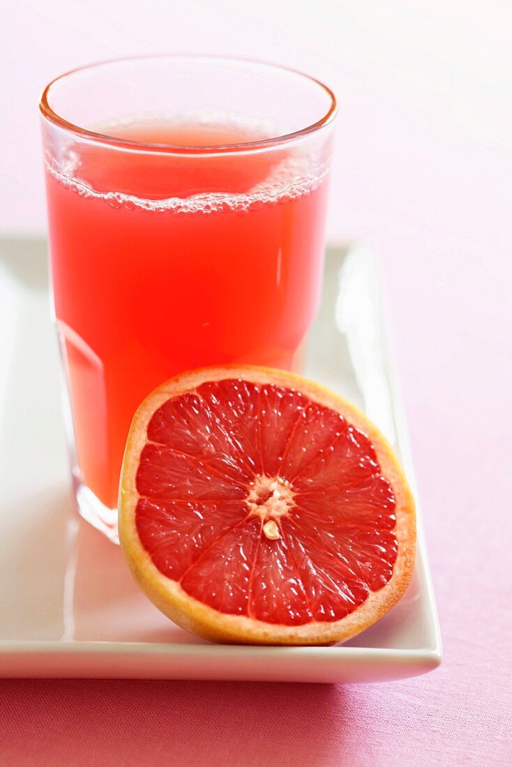 Ein Glas rosa Grapefruitsaft und halbe Grapefruit