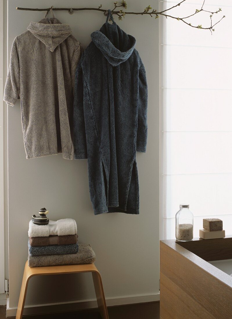 Two dressing gowns hanging on wall above stacked towels on stool