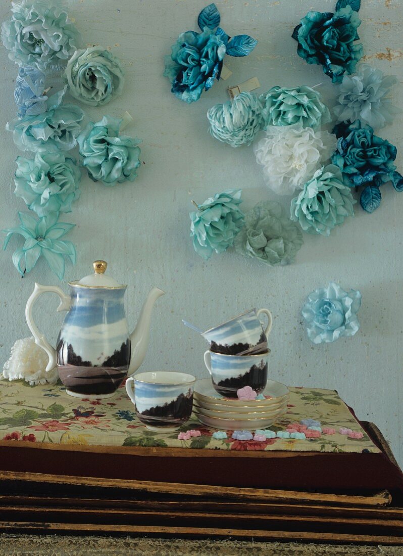 Bemalte Kaffeeservice vor türkisfarbener Wand mit Stoffblumen