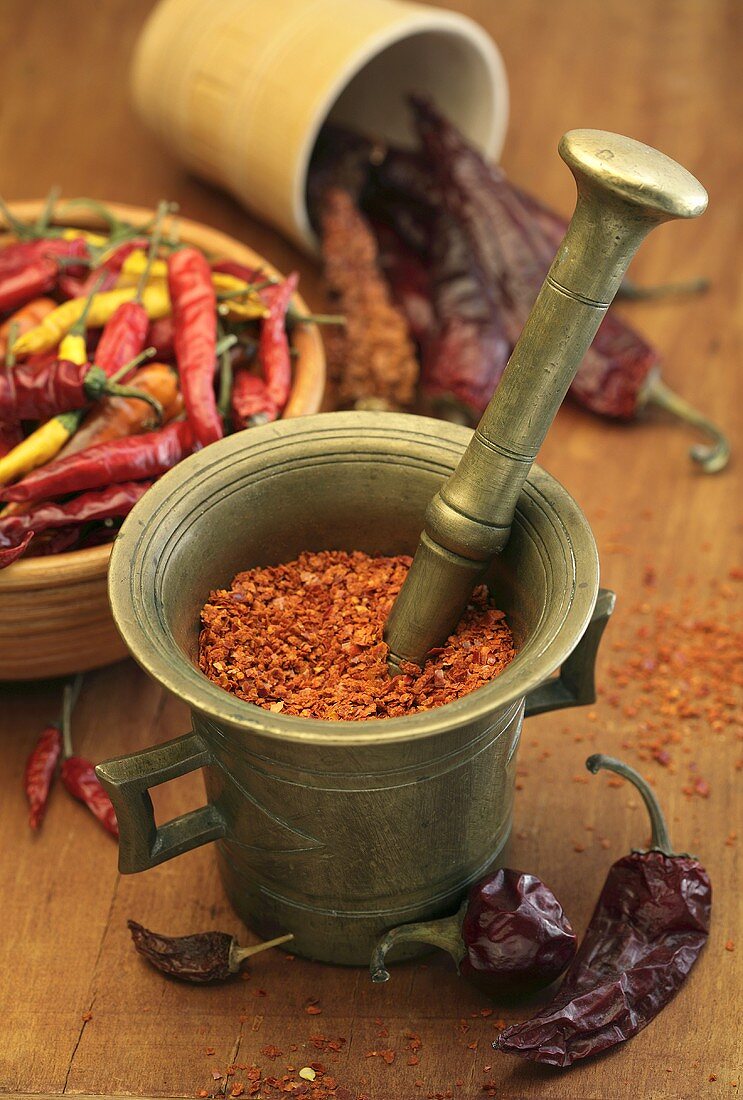 Chilli flakes in a mortar with various types of chilli peppers