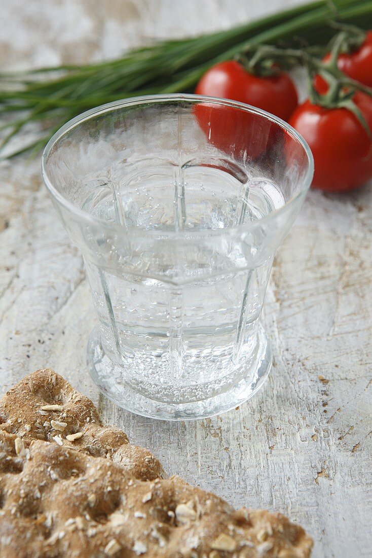 Wasserglas, Knäckebrot, Tomaten und Schnittlauch